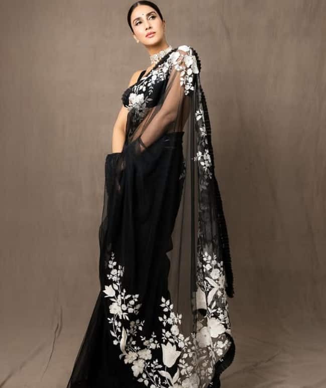 Vani Kapoor looks beautiful in white flowers embroidery and fine detailing transparent black saree. His sleeveless blouse is giving modern touch to his look. With this, he is wearing a silver statement. At the same time, his slick bun has added to his beauty.