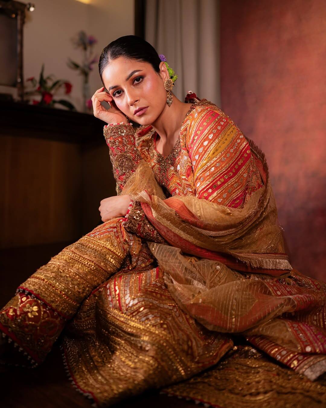 In this look, Shahnaz is seen in an ethnic look. He is wearing golden and red huge embroidered ethnic outfits. There are matching scarf and earrings with Kurta. Hair has been tied back and natural makeup is completing this look.