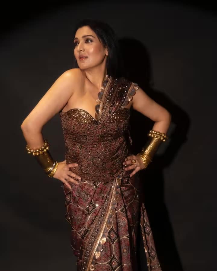 भूरे रंग के इंडो-वेस्टर्न आउटफिट में टीना आहूजा का लुक बेहद रॉयल और अनोखा है। गोल्डन ज्वेलरी उनके स्टाइल को और भी खूबसूरत बना रही है। अपने हेयरस्टाइल को सिंपल रखते हुए उन्होंने अपने आउटफिट को आकर्षण का केंद्र बना दिया है।