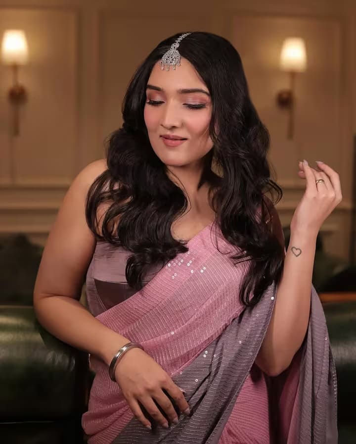 टीना आहूजा गुलाबी रंग की चमकदार साड़ी में बेहद खूबसूरत लग रही हैं। माथे पर बैंग्स और सॉफ्ट कर्ल हेयरस्टाइल उनके पारंपरिक लुक को और भी शाही बना रहे हैं। उनकी प्यारी सी मुस्कान इस तस्वीर को एकदम परफेक्ट बना रही है।