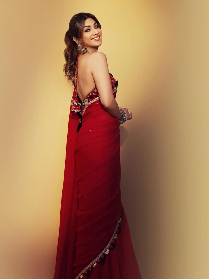 In this photo, Shilpa is wearing a beautiful red color saree, which has a detailing of golden and dark shades on the border. She has paired backless blouse with saree. He has completed his look by tying the hair in a ponytail with light curls and wearing big earrings.