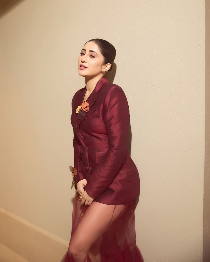 In this look, Shivangi is wearing a dark maroon -colored outfit, which has a trail made of blazer style top and net fabric. Flower detailing is made on the outfit. They have tied the hair in a clean way, with light makeup and nude lipshade, they have kept their look minimal. The statement earpiece worn in the ears is giving a glamorous touch to this entire look.