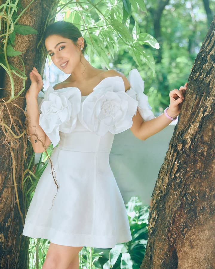 इस लुक में सारा ने सफेद ऑफ-शोल्डर ड्रेस पहनी है, जिस पर बड़े-बड़े 3डी फ्लोरल डिटेल्स हैं. नेचुरल लाइट और ग्रीनरी के बीच उनका यह लुक बेहद फ्रेश और फेयरी-स्टाइल वाइब देता है. सिंपल मेकअप और टाई किया हुआ हेयरस्टाइल उनकी लुक को पूरा कर रहा है.