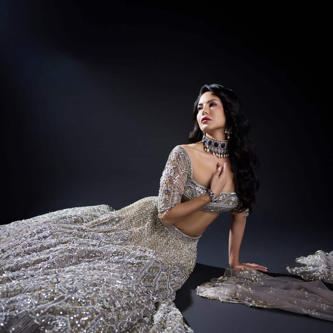 In this look, Sunny Leone is wearing a silver lehenga with heavy embroidery, which is styled with statement jewelery and open hair. His look is giving a very traditional vibe.