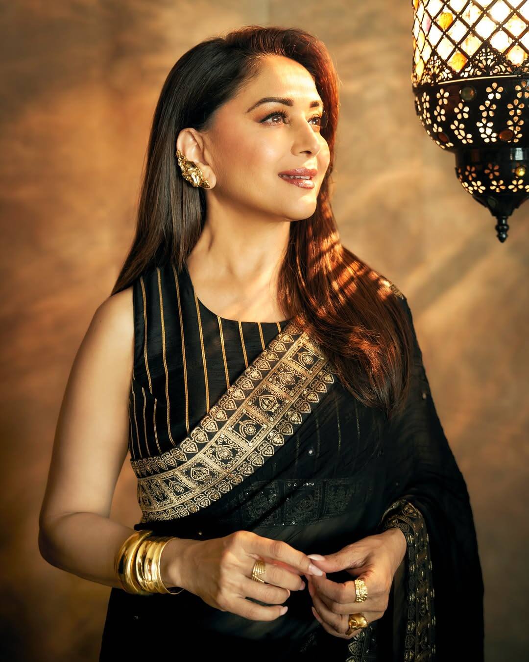 Madhuri's blouse style is very classy in this look. It is a sleeveless blouse, whose neckline is in close round neck style. The design has a pattern of golden vertical strips, giving the blouse a slim fit look. The cut and fitting of the blouse is absolutely simple, but with the golden border of the saree, its combination is giving festive touch.