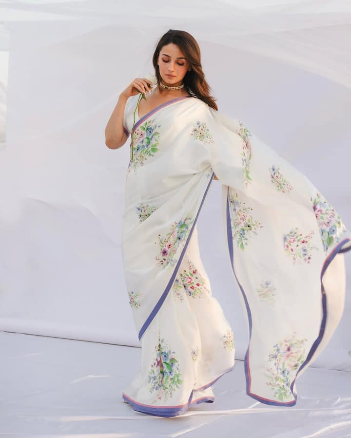आलिया ने इस लुक में सफेद रंग की फ्लोरल प्रिंट साड़ी पहनी है, जिस पर हल्के और सॉफ्ट रंगों का काम है. साड़ी का पर्पल बॉर्डर है. उन्होंने मिनिमल मेकअप, ओपन हेयर और सिंपल चोकर नेकलेस के साथ अपने लुक को पूरा किया है. यह अंदाज़ एकदम सॉफ्ट और फ्रेश वाइब दे रहा है.