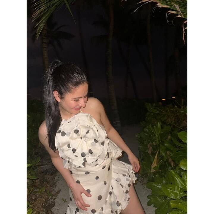 Katrina is wearing a black-white polka dot mini dress in this picture. There are large floral designs and frill details on the dress. His style looks very fresh with a ponytail hairstyle and natural look.