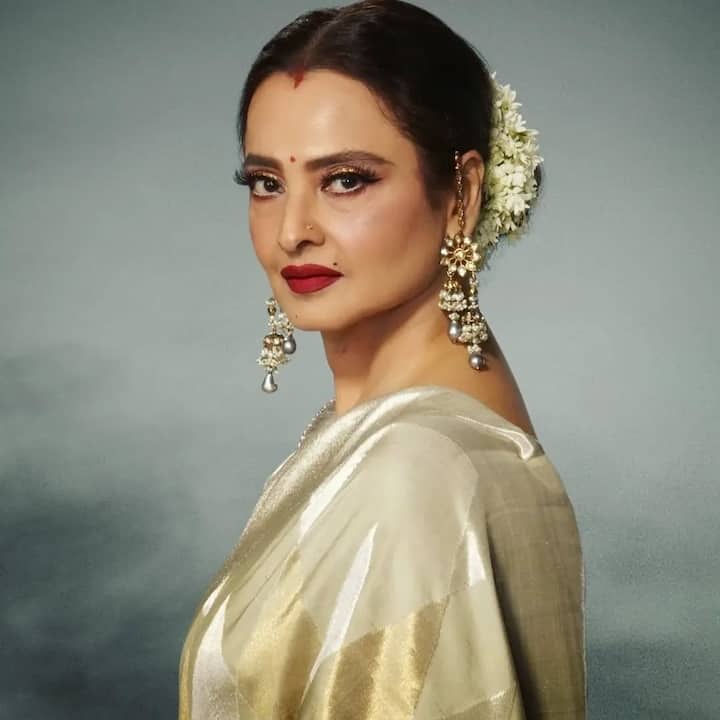 इस तस्वीर मे रेखा ने गोल्डन रेशमी साड़ी पहनी है, जिसे गजरे से सजे क्लासिक हेयरबन और बड़े झुमकों ने पूरा किया. लाल बिंदी, लाल लिपस्टिक और सटल मेकअप उनके ट्रेडिशनल अंदाज़ को बेहद खूबसूरत और रॉयल टच दे रहे हैं.