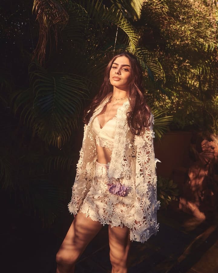 This look of Khushi Kapoor is giving very driem and fresh vibe. He is wearing a white floral lace co-ord set, which includes Bralet, shorts and matching capes. The outfit is giving them modern and boho touch. Soft makeup and open hair are making this look natural and elegant. This look between sunlight and greenery looks absolutely refreshed and glamorous.