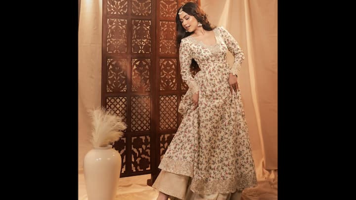 1. Muted Floral Anarkali: Reem Shaikh radiates timeless charm in this ivory floral Anarkali that’s perfect for festive occasions. The outfit features delicate pink and green floral prints, paired with intricately lace detailing. Styled with a rich golden flared bottom and a traditional maang tikka, her look beautifully blends modern sophistication with ethnic tradition. The pastel tones and flowing silhouette make it a versatile festive wardrobe pick. (Image Source: Instagram/@reem_sameer8)