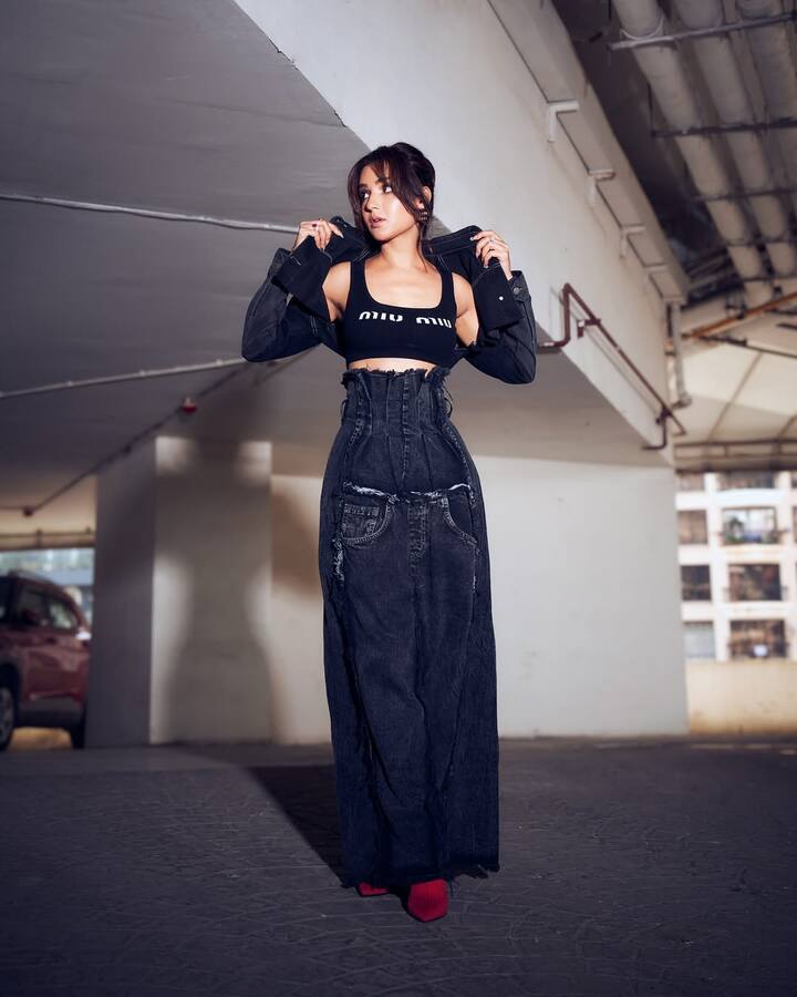 In this picture, Jasmine is wearing a Black Bralet, denim jacket and high-wested long denim skirt. This style is giving modern streetwear vibe. Red heels are giving contrast and statement touch to the entire outfit. His look is aged and fashion-forward.