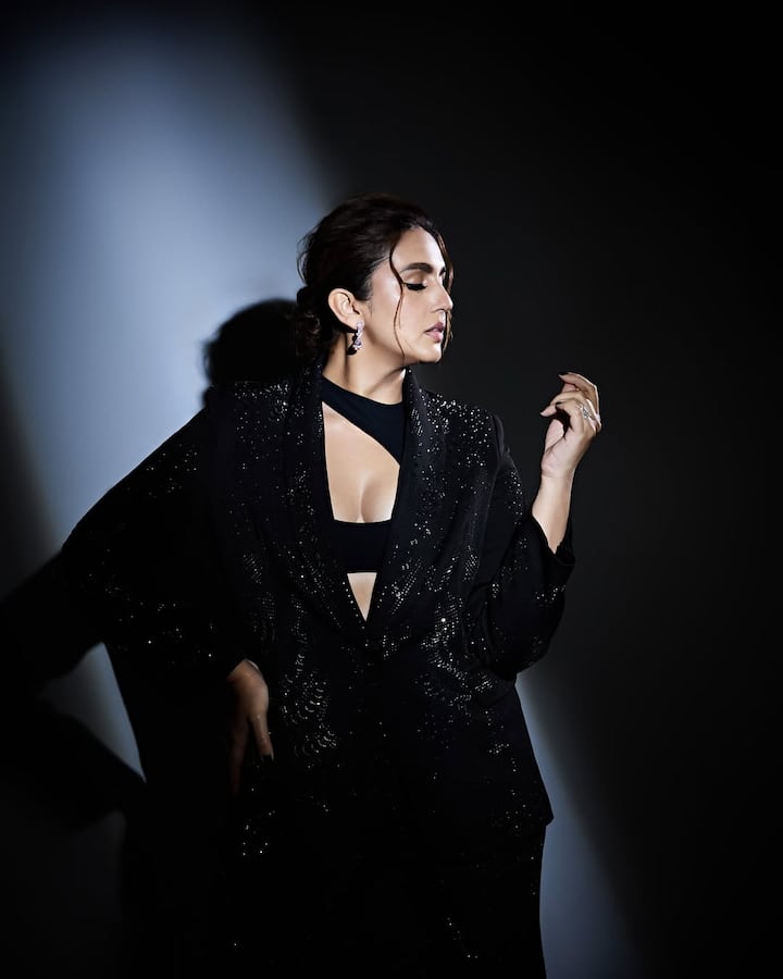 Huma Qureshi, wearing a shiny blazer-pants with a black colored brlate, looks quite stunning. His hairstyle and pose are giving him a stylish touch.