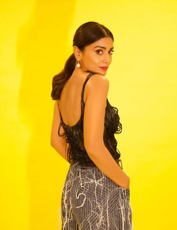 Black laces is wearing top and stylish gray pants, which has white unique design. This look with yellow background shows modern and fashionable style well.
