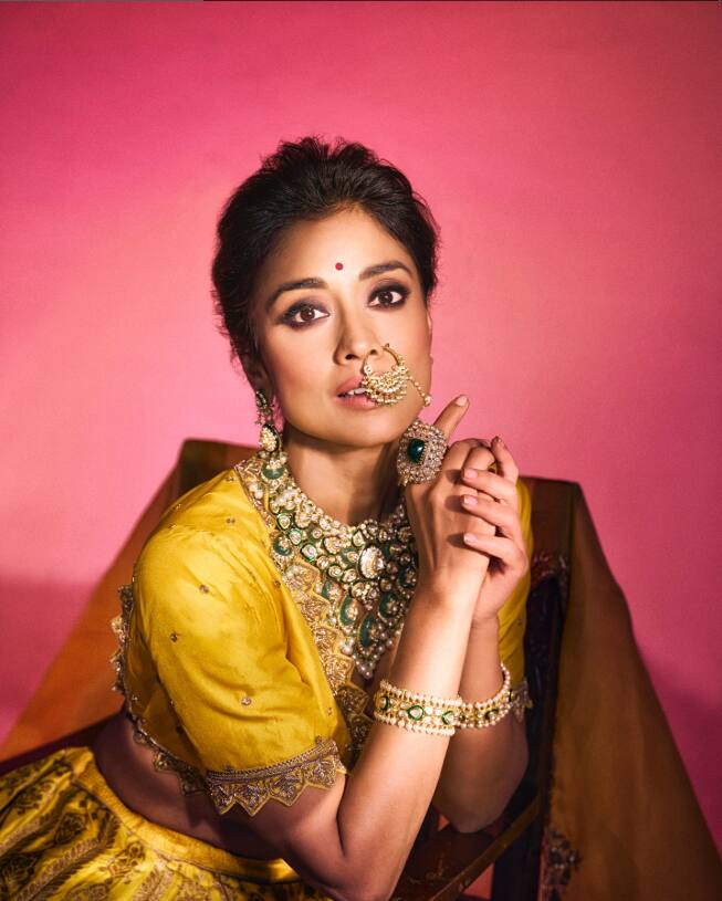 In this picture, it is adorned in the traditional Indian look, she looks very beautiful in yellow lehenga and heavy jewelery. She is posing in a cultural and royal style with Nath, necklace, bangle and ring.