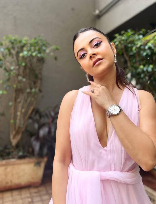 देवोलिना लाइट पिंक डीप नेक गाउन में काफी प्यारी और स्टाइलिश नजर आ रही हैं. शार्प आई मेकअप, वॉच और पोनीटेल उनके लुक को और भी ट्रेंडी बना रहे हैं.