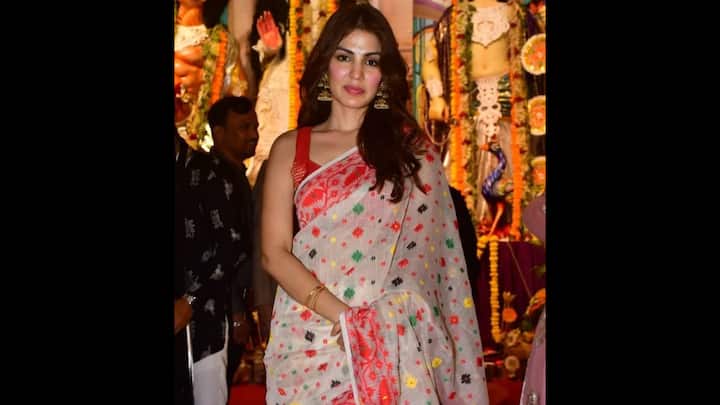 2. Rhea Chakraborty: Rhea Chakraborty showcased a look that was both deeply rooted in culture and effortlessly elegant. She opted for a handloom saree that was a perfect blend of simplicity and charm. The crisp white fabric with its intricate, multi-colored motifs was a breath of fresh air, while the traditional red border added a classic, festive touch. The statement temple jhumkas and traditional bangles perfectly complemented the ethnic vibe of the saree. This look is a fantastic example of how to honor tradition while adding a touch of personal style. (Image Source: Pinterest/marigoldaustin)