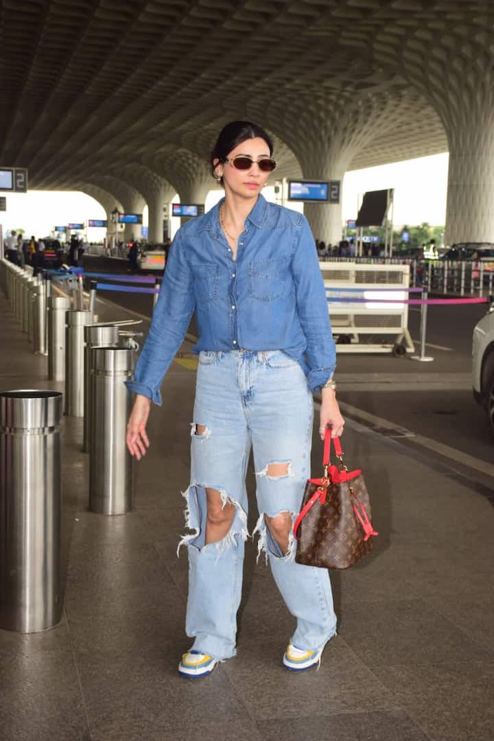 This airport look of Daisy Shah is trendy and casual. He has adopted a denim-on-denim style wearing a ripped denim jeans with a blue denim shirt. Colorful sneakers and brown-red combo bags are making their look more stylish. Sunglasses are doing cool touch in it.