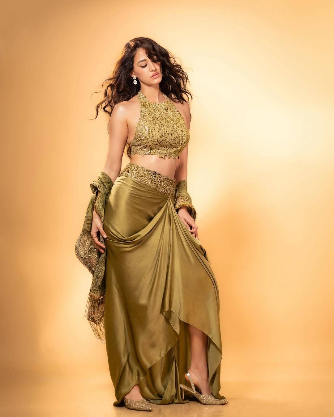 In this picture, Disha is wearing a brilliant golden color two-piece outfit. This outfit has a top and high-slit skirt with halter neck. In this look, Disha is looking very glamorous.