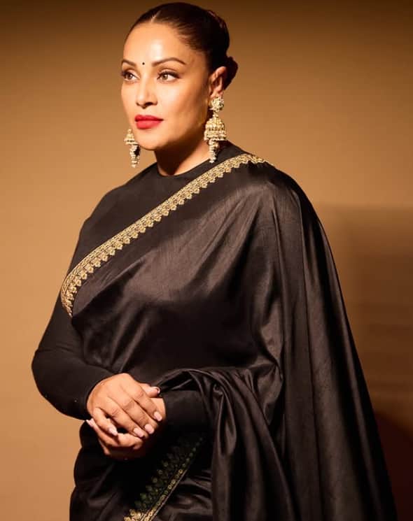 In this picture, the black color saree is seen wearing with a golden border which is very much enhancing her look, as well as heavy earrings and red lipstick is making her look even more elegant.