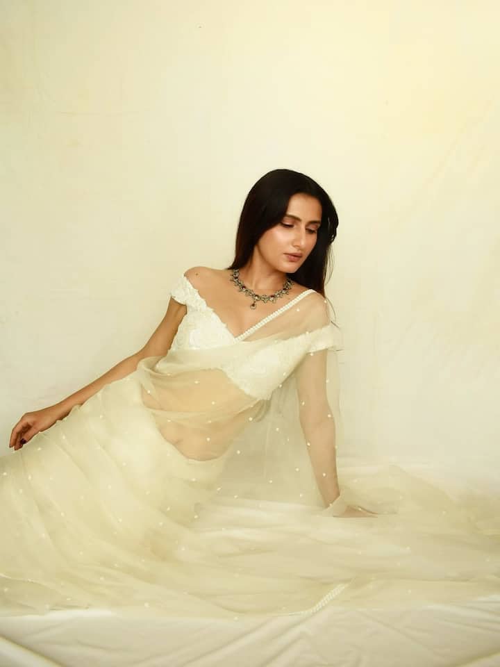 Fatima is wearing a white net saree in this look. Off-shoulder blouses, minimal makeup and silver neckpiece are making his look a graceful and elegant.
