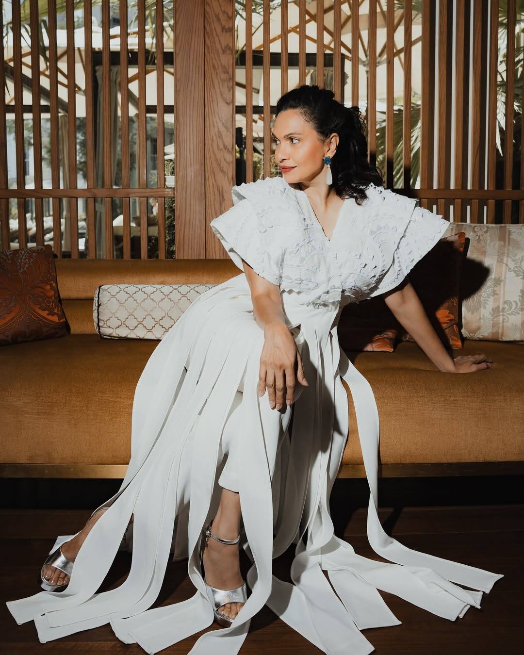 Maria is wearing a white drape-style outfit in this look. Silver heels and statement earrings are making their look even more glamorous. His look looks modern with sleek hairstyle and soft makeup.