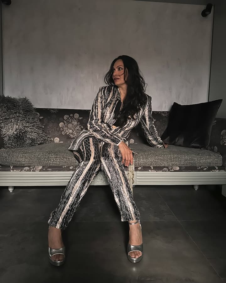 In this picture, Maria is wearing Shiney Black-Goldish Pantsuit. They have carried silver heels with it. Open hair and minimal makeup are balanced by their look. This look of Maria is stylish and glamorous.