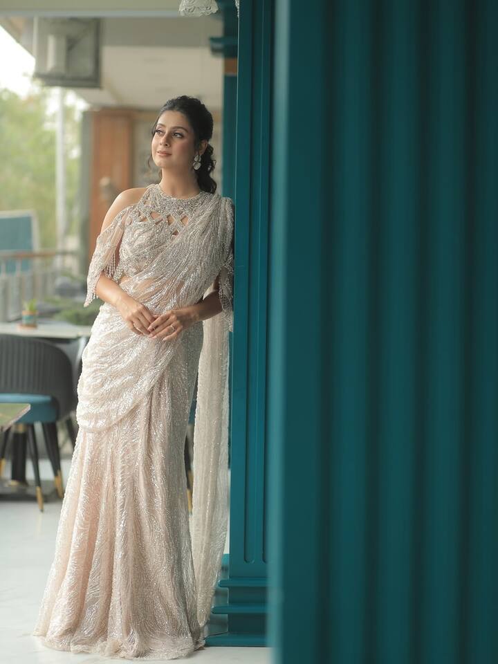 इस लुक में ईशा ने शिमरी ऑफ-व्हाइट साड़ी पहनी है, जिसे मॉडर्न कट-वर्क ब्लाउज़ के साथ स्टाइल किया गया है. मिनिमल ज्वेलरी और सॉफ्ट मेकअप उनके आउटफिट को और भी ग्रेसफुल बना रहे हैं. खुली वेव्स वाली हेयरस्टाइल लुक में एलिगेंस जोड़ती है.