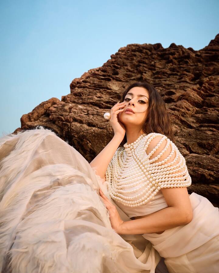 ईशा ने इस लुक मे ऑफ-व्हाइट साड़ी के साथ पर्ल ड्रेप्ड स्टेटमेंट ब्लाउज कैरी किया है. मिनिमल मेकअप और ओपन हेयरस्टाइल उनके लुक को नैचुरल लेकिन ग्लैमरस टच दे रहा है.