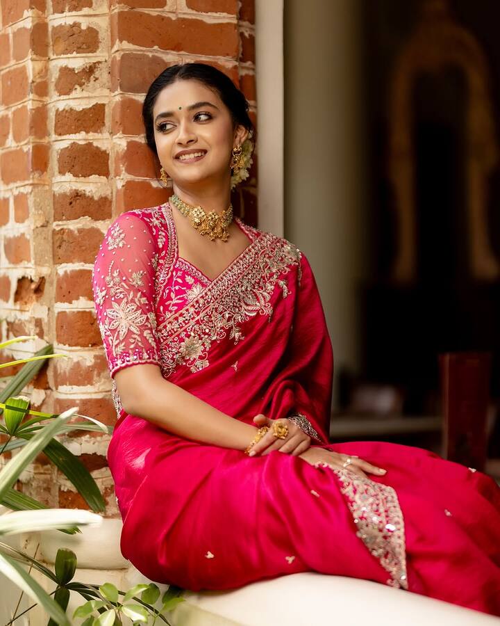 Turn heads like Keerthy in a stunning red silk saree with golden embellishments and intricate borders. Pair it with a heavily embroidered halter-neck blouse and finish the goddess-like look with a golden choker, statement jhumkas, and a neatly tied bun wrapped in fresh gajra.
