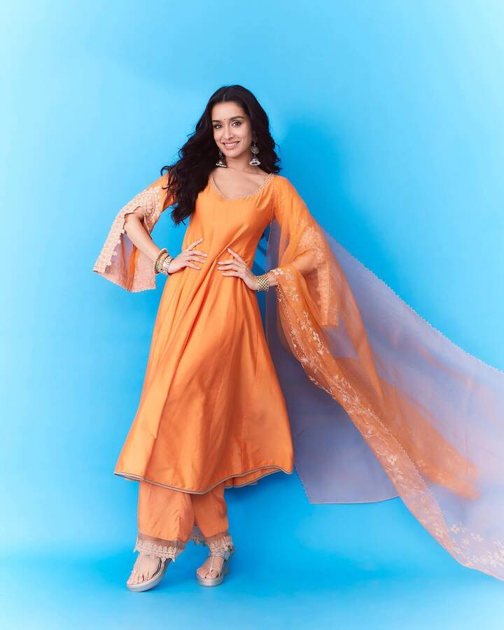 Shraddha is wearing a beautiful salwar suit of dark orange colored in this look. There is a lace border on a matching pants with flair -with kurta and wide lace sleeves, paired with light net and embroidered dupattas. Big earrings, bangles and heels are completing their look.