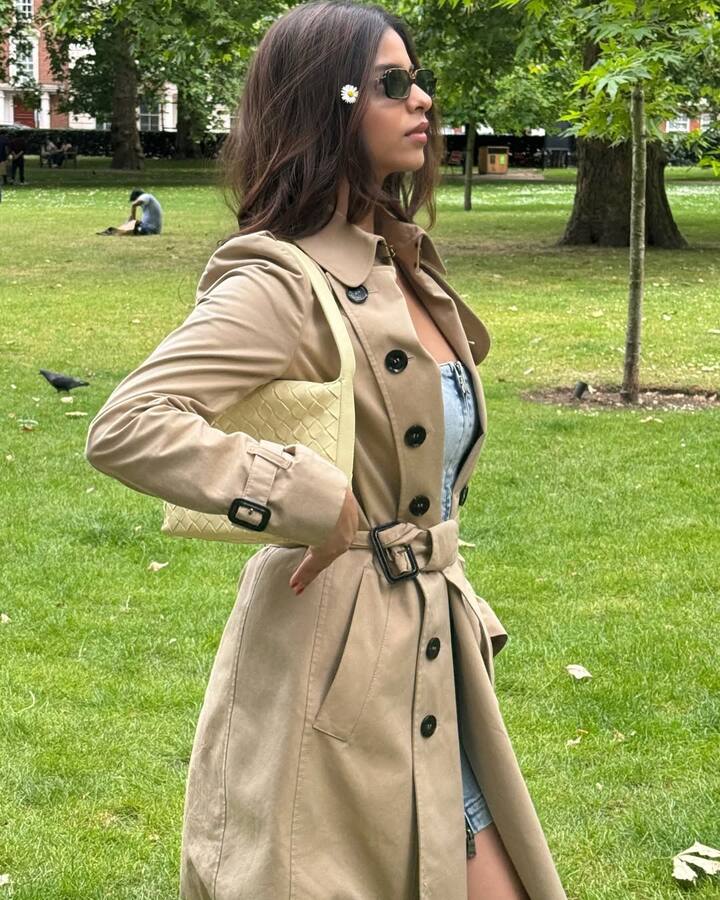 In this picture, Suhana is wearing a beige trench coat, which has been fitted with the belt. There is a glimpse of a denim dress inside, which is giving a casual touch to the look. Light yellow bag, black sunglasses and white flowers in hair are further enhancing their elegance on the shoulder. This look is smart, modern and elegant.