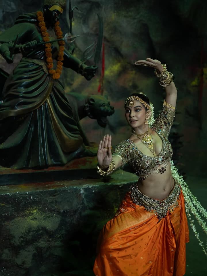 In this look, Jacqueline is seen in the look of a traditional dancer. He is wearing a golden -working heavy blouse and an orange silk lehenga dhoti style. Heavy gold jewelery, mathpatti, bracelet and gajra fill their looks with extremely royal and divinity.