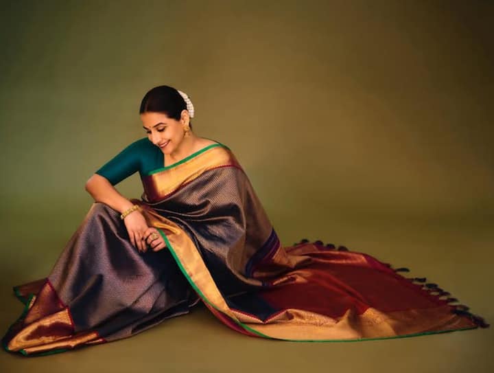 इस तस्वीर में विद्या बालन ग्रीन ब्लाउज और गहरे रंग की ट्रेडिशनल साड़ी में मुस्कुराते हुए पोज दे रही हैं. जूड़े में गजरा और गोल्डन ज्वेलरी उनके लुक को और क्लासिक बना रहे हैं.