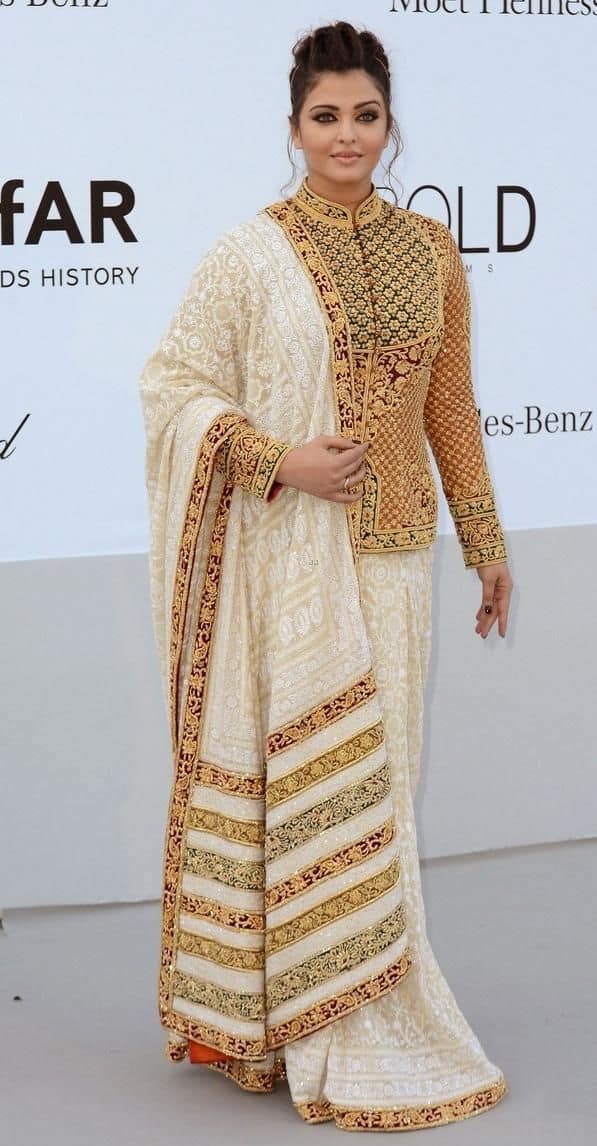 Aishwarya is wearing a brilliant ethnic outfit of white and golden color in this photo. She is wearing a white colored saree and a long jacket-style blouse on it. This blouse is decorated with golden and black embroidery. He has completed this look with a matching dupatta, which has red and golden colored work on the border. His hair is tied in one bun and his makeup is neutral, which is drawing attention to his outfit.