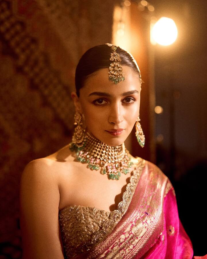 In this picture, Alia is wearing a pink silk saree. He has pair it with an off-shoulder blouse in a golden color. This blouse has a fine embroidery and zari work with golden threads, which is giving it a very rich and elegant look. The design of the blouse is giving a modern and stylish appeal to leave the neckline completely open, which looks very beautiful with a traditional saree.