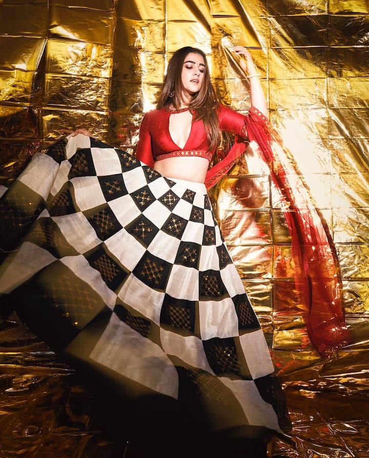 In this picture, Nupur is wearing a very stylish and modern lehenga. His blouse is dark red, which has a deep-neck design. The pattern of his lehenga is quite unique, which has a checkerboard print of black, white and golden colors. He has completed his outfit with a thin, red colored dupatta.