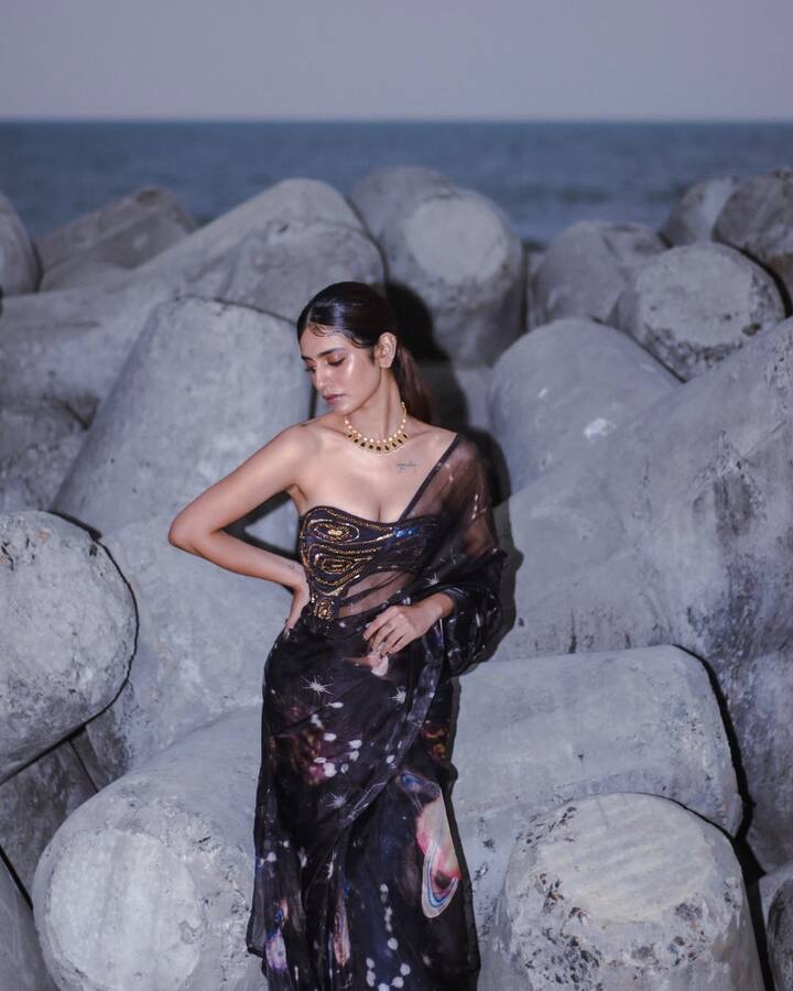 Priya, wearing a black color transparent saree and off shoulder blouse, looks very glamorous. White and Black Necklace is completing his look.