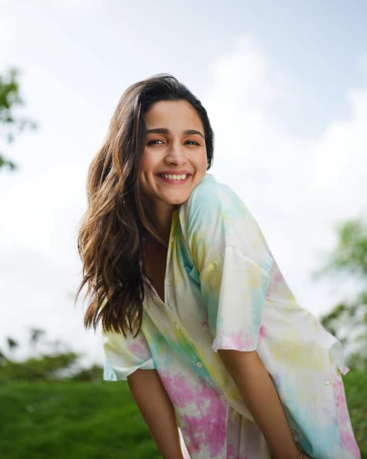इस लुक मे आलिया एक रिलैक्स्ड और समर-फ्रेंडली वाईब दे रही है. उन्होंने एक मल्टीकलर टाई-डाई प्रिंट वाली ओवरसाइज़्ड शर्ट पहनी हुई है, जिसमें हल्के गुलाबी, पीला, और नीला रंग शामिल है. उनके बाल खुले, हल्के वेवी हैं. उन्होंने नो-मेकअप लुक रखा है, जो उनकी स्माइल को हाइलाइट कर रहा है. यह लुक किसी आउटडोर, पिकनिक या गार्डन सेटिंग के लिए परफेक्ट है.