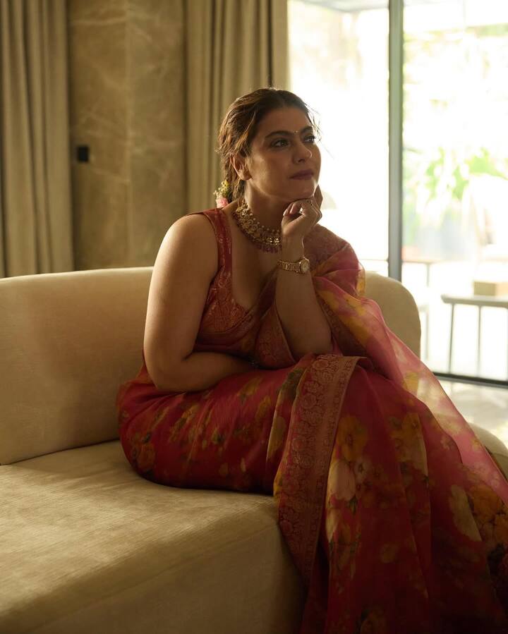 काजोल इस लुक में बेहद एलीगेंट और ग्रेसफुल नजर आ रही हैं. उन्होंने गहरे गुलाबी-लाल रंग की फ्लोरल प्रिंट वाली साड़ी पहनी है, जिसे मैचिंग डीप नेकलाइन वाले स्लीवलेस ब्लाउज़ के साथ कैरी किया है. उनके लुक को हैवी स्टोन चोकर नेकलेस और गोल्ड वॉच ने और भी रॉयल टच दिया है. मेकअप सॉफ्ट और न्यूड टोन में है, जिससे उनका नेचुरल ग्लो हाईलाइट हो रहा है. बालों को सिम्पल बन में उन्होंने रखा है.