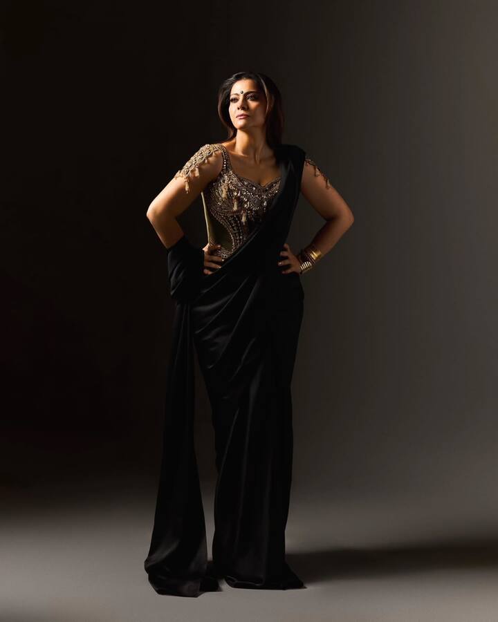 Here Kajol is in a stylish and modern look, in which she is wearing a black saree. She has paired this saree with a very beautiful blouse. This blouse is golden colored and an intricate embroidery has been done on it. The shoulder strap of the blouse has also been installed, which is making their look special. In the accessories, he is wearing gold bracelets and earrings. Their hair is open and makeup is light, which is making this look even more attractive.