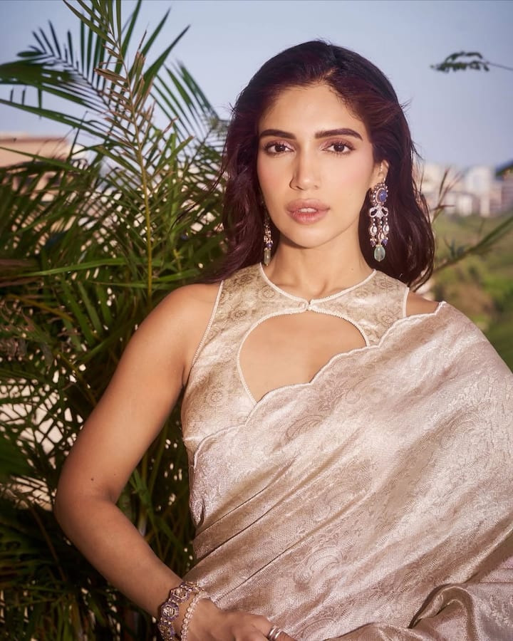 भूमि पेडनेकर का यह एक गोल्डन-ऑफ-व्हाइट कलर का स्लीवलेस ब्लाउज है. इसकी सबसे खास बात इसका नेकलाइन डिज़ाइन है, जो सर्कल शेप का है, और गले के पास एक बटन लगा है. इस पर बारीक गोल्डन कलर का काम है, जो इसे क्लासी लुक दे रहा है. इस तरह का ब्लाउज डिज़ाइन उनके लिए परफेक्ट है जो करवा चौथ पर ट्रेडिशनल और एलिगेंट लुक चाहती हैं.