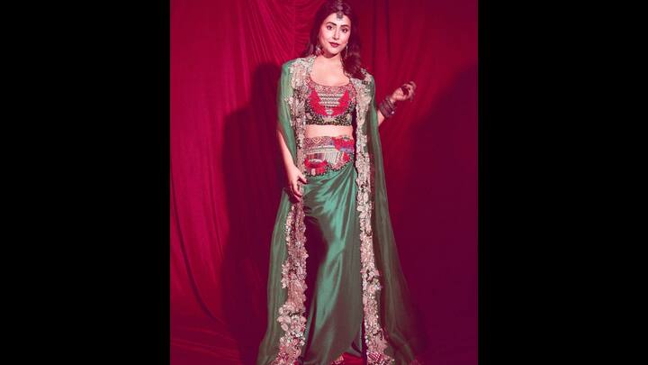 2. Emerald Green Lehenga: Hina Khan dazzles in an emerald green lehenga paired with a heavily embellished floral blouse and ornate belt detailing. The look is elevated with a sheer embroidered cape, replacing the traditional dupatta with a contemporary twist. Accentuated by statement earrings and a maang tikka, this outfit blends regal charm with bold festive vibes. (Image Source: Instagram/@realhinakhan)