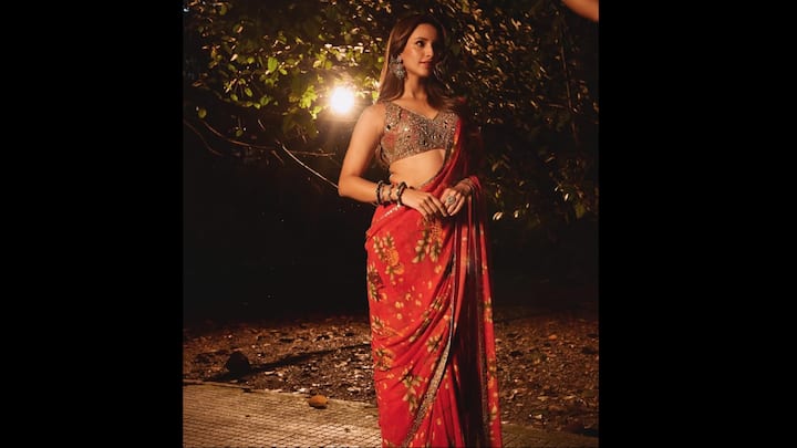 6. ⁠Tripti Dimri: Tripti wears a gorgeous red saree, serving a glamorous look. What makes this look exceptional for Karwa Chauth 2025 is the unexpected addition of a delicate floral print against the auspicious red hue. This print introduces a subtle, modern femininity that prevents the traditional red from feeling too heavy. The true style statement is the accompanying blouse. Tripti pairs her floral drape with a spectacular, heavily-embellished mirror work blouse. Opting for a sleeveless or V-neck cut, the blouse provides a dazzling contrast to the saree's flowing print. The sparkle instantly elevates the ensemble from casual chic to celebratory grandeur, making it perfectly puja-ready. (Image Source: Instagram/@tripti_dimri)