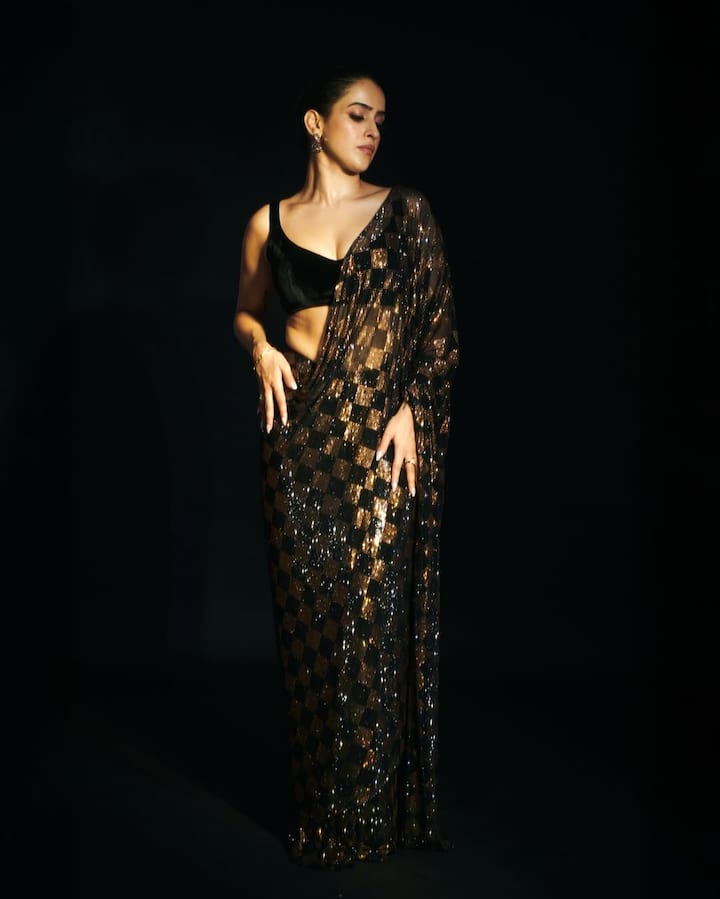 In this look, Sanya has brought a fantastic and glamorous option for festive season and parties. She is wearing a black and gold -colored shimri sequence saree, with a checkerboard pattern. This saree will look very good in the night function. She has paired the saree with the deep-neck black blouse of Velvet. The accessories have simple stud earrings and sleek bracelets, which are not allowing the brightness of the saree to dominate. Hair tight and minimal makeup is completing this look, which is perfect for Diwali or any grand event.