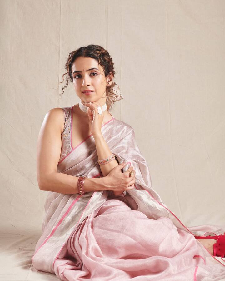 Sanya Malhotra is wearing a baby pink colored orgenza saree in this look, which has a thin border of silver and zari. She has paired the saree with sleeveless, embroidered blouse. Their white bran and colorful bracelets are filling color and glow in this conference look. Open curls in the hair and instead of gajra, satin bo is giving it a modern and romantic touch. This look is perfect for festivals where you want to show more grace than glamor.