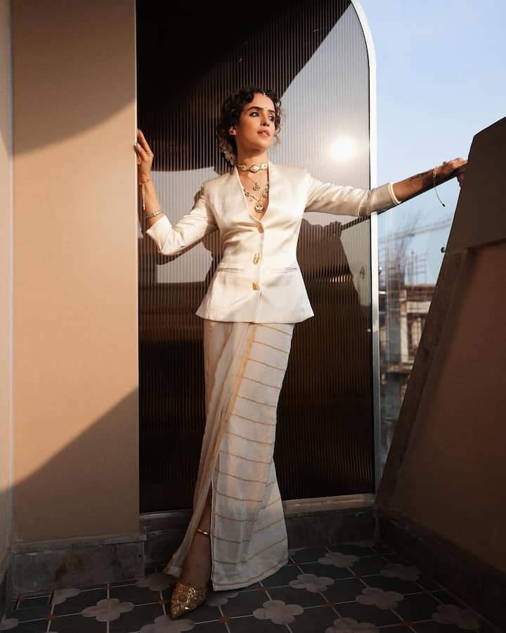 This look of Sanya is a unique and contemporary fusion for the festive season. She is wearing an ivory color satin blazer, under which the golden border is an off-white dhoti skirt. This western blazer and traditional dhoti mix is making it very special. He has styled this look with traditional golden choker, long necklaces and pointed golden shoes. This is excellent for those parties where you want to look powerful and ethnic-modern.