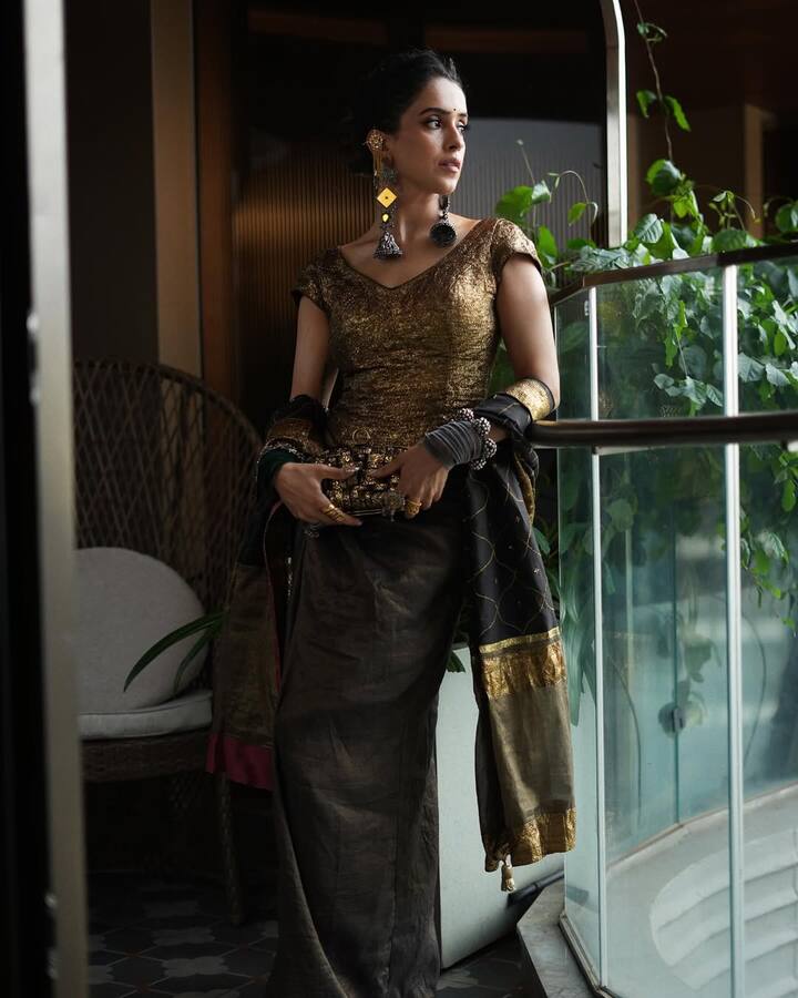 This look of Sanya is perfect inspiration for the festive season. She has paired golden blouse and dark silk saree with black and gold border dupattas. Heavy earrings, cuff bangles and statement jewelery are giving their look to royal and traditional touch. Simple makeup and tied hair further enhance their elegance, causing this outfit modern as well as classy.