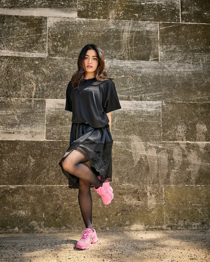 In this look, Rashika has carried an all-black trendy look. He is wearing a loose black T-shirt, below which is a black lace detailing skirt. They have black sheer stockings in their feet, giving this look a western touch. But the most special is to wear their bright pink sneakers, who are making a funky contrast with full black outfits. With open hair and a stylish pose, this look is very cool and fashion-forward.