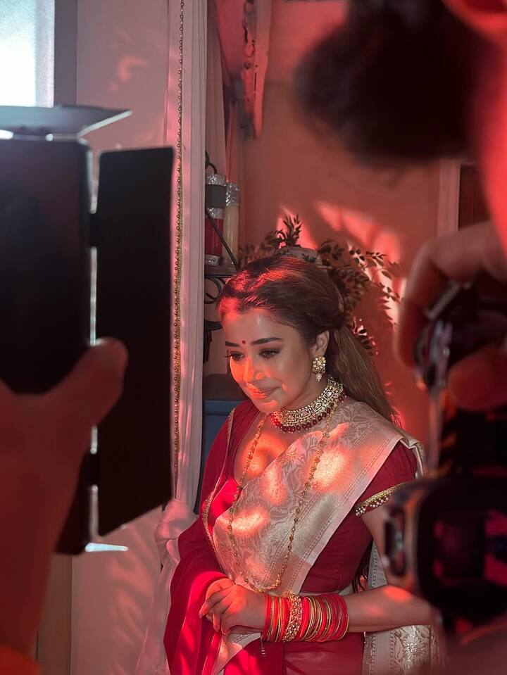 Tina’s makeup is flawlessly minimal yet striking — dewy skin, soft coral lips, kohl-rimmed eyes, and a gentle highlighter that accentuates her cheekbones under the warm lighting. The tiny red bindi adds a touch of traditional sensibility to her radiant look.