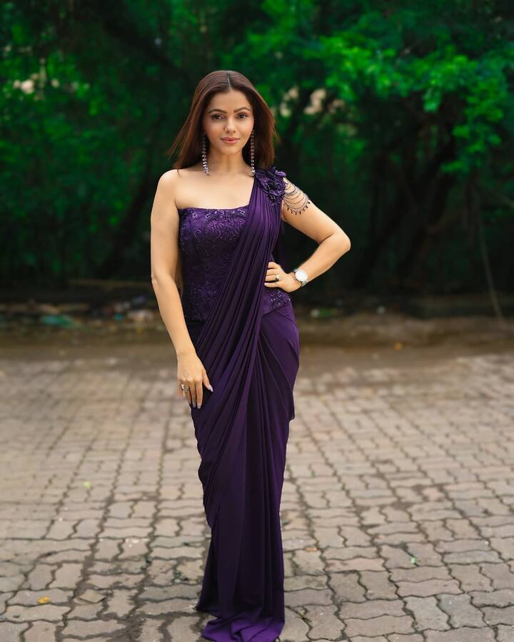 रुबीना का यह पर्पल प्री-ड्रेप्ड साड़ी लुक करवा चौथ के लिए बेहद रॉयल और मॉडर्न है. उन्होंने गहरे पर्पल रंग की रेडी-टू-वियर साड़ी पहनी है, जिसे वन-शोल्डर एम्ब्रॉयडरी वाले ब्लाउज के साथ स्टाइल किया है. कंधे पर लगी बीडेड एक्सेसरी और स्टाइलिश झुमके इस पूरे लुक को एलिगेंट बना रहे हैं.